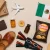 Mexican products including leather sandals, Sabritas chips, candy, supplements, a woven textile, and cardboard shipping boxes arranged with a toy airplane and Mexican flag